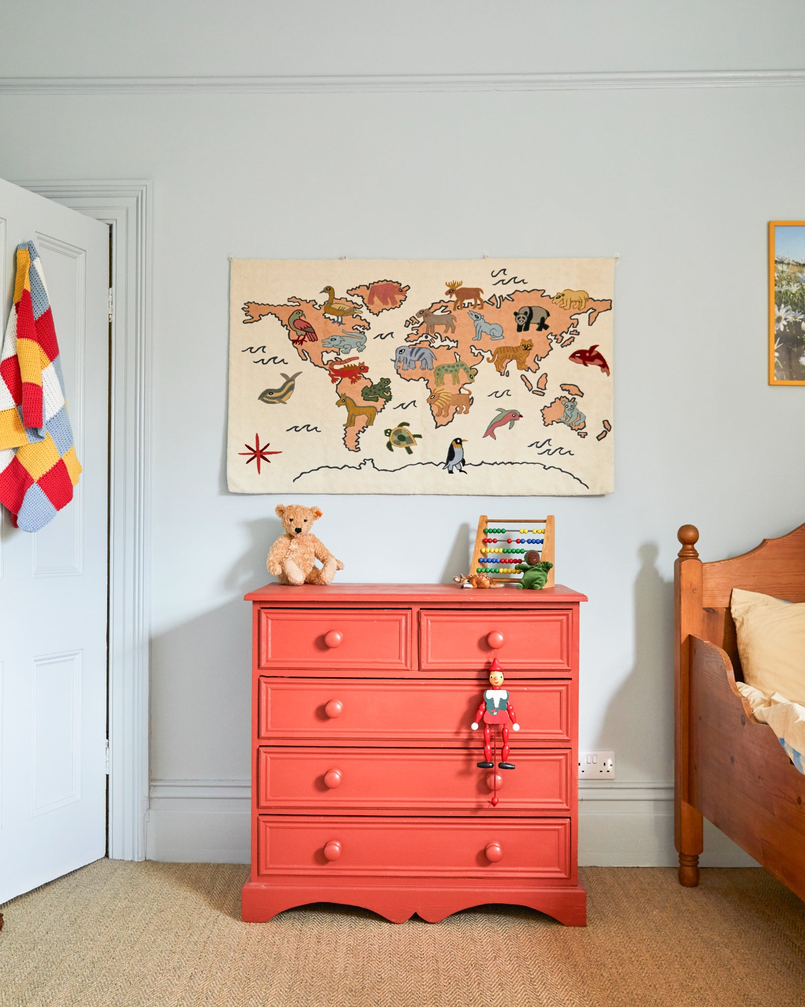 Red dresser with toys in a child's room featuring a world map on the wall.