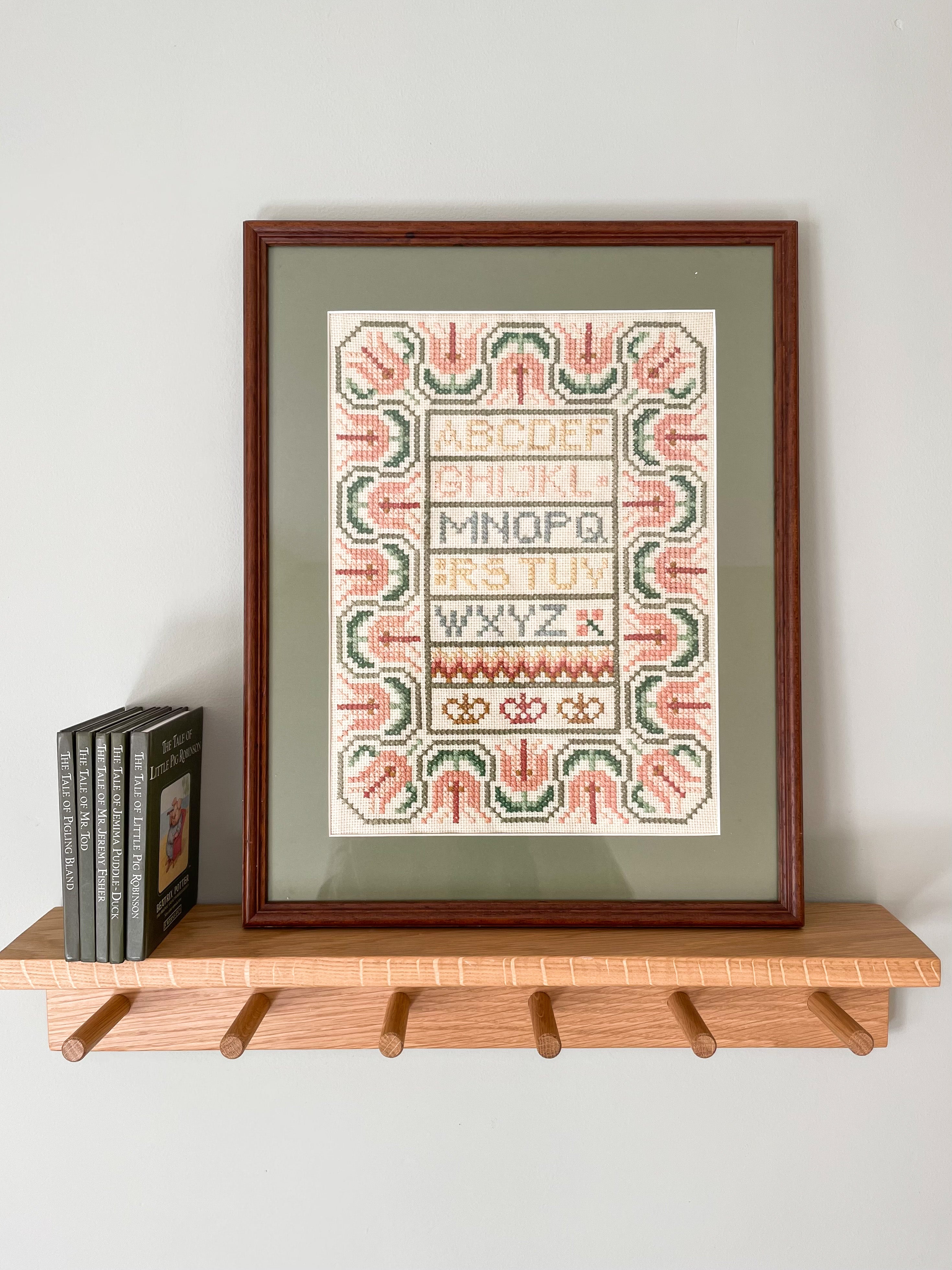 Vintage framed embroidery featuring an alphabet design in pastel colours with a green mount - Moppet