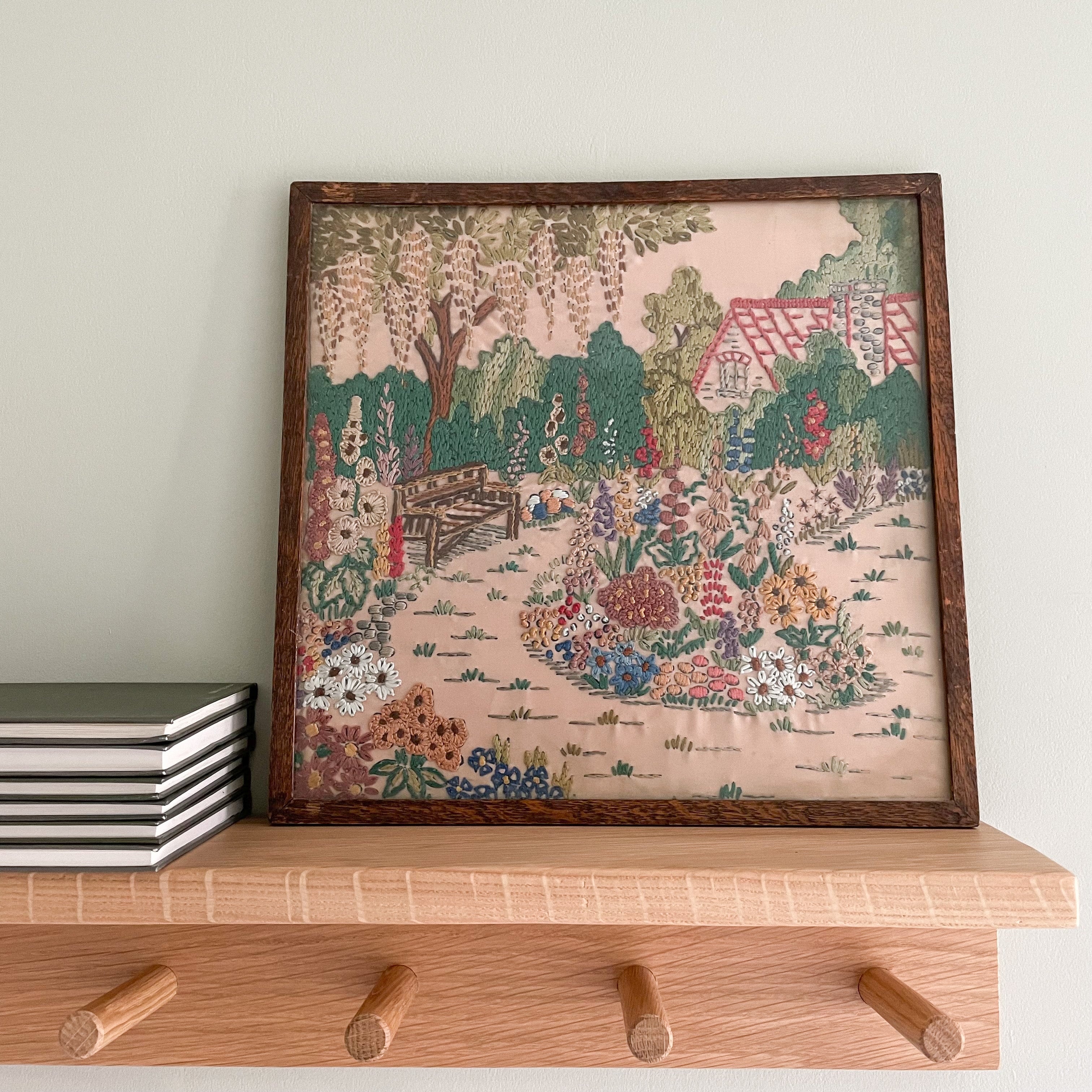 Vintage framed embroidery of a garden, house and bench, blush pink background - Moppet