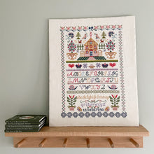 Load image into Gallery viewer, Vintage cross stitch sampler of a house and alphabet in a rainbow of muted pastels - Moppet
