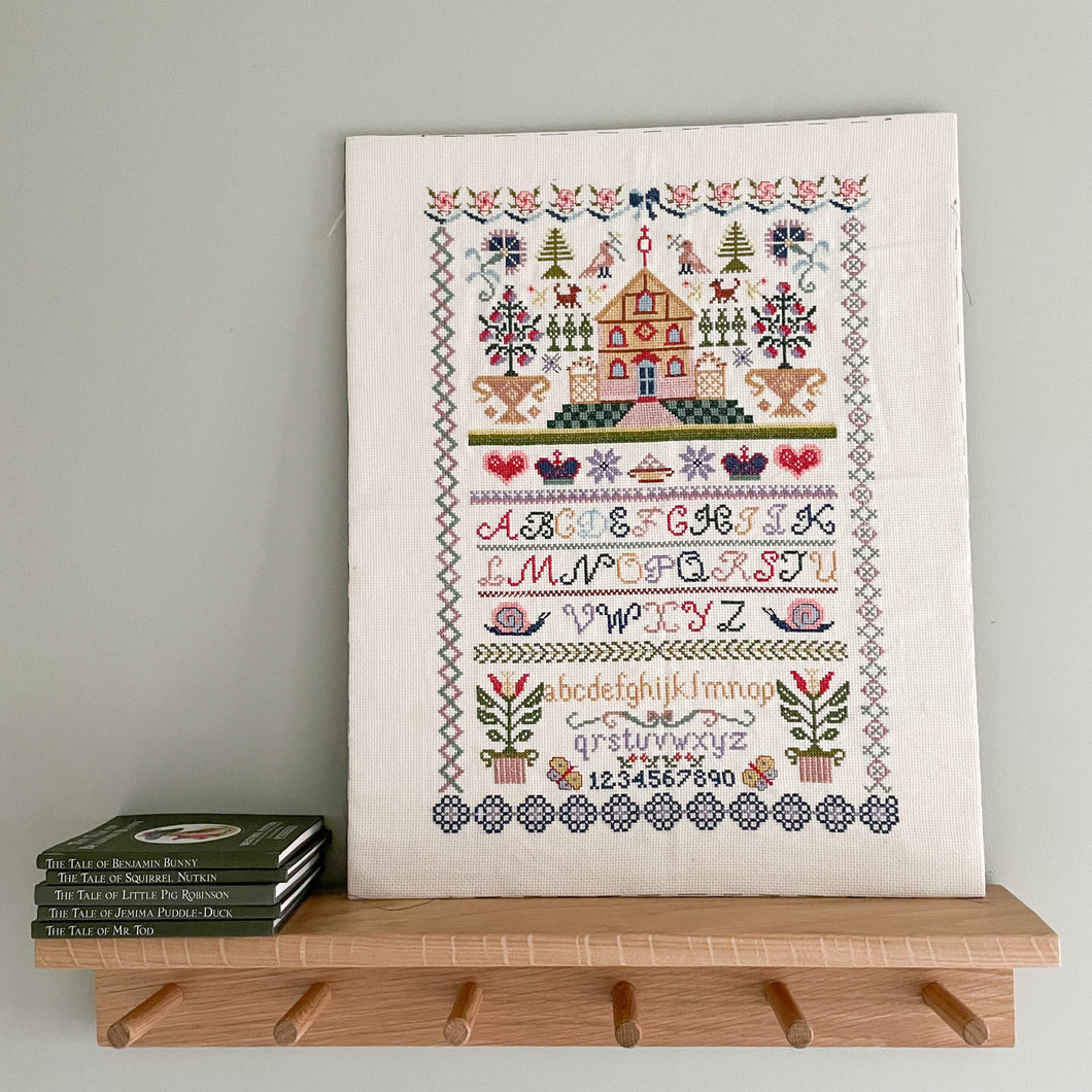 Vintage cross stitch sampler of a house and alphabet in a rainbow of muted pastels - Moppet