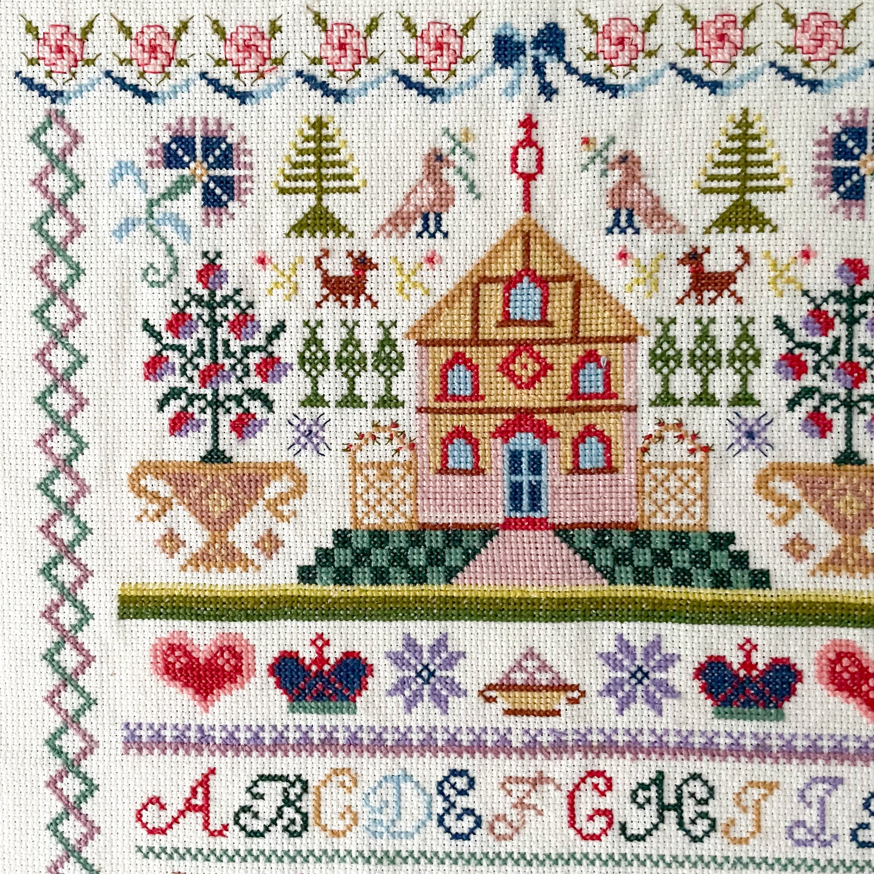 Vintage cross stitch sampler of a house and alphabet in a rainbow of muted pastels - Moppet