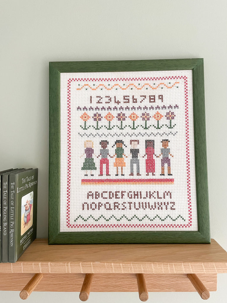 Vintage framed children's embroidery or needlework alphabet sampler featuring a row of children holding hands in a green wooden frame - Moppet