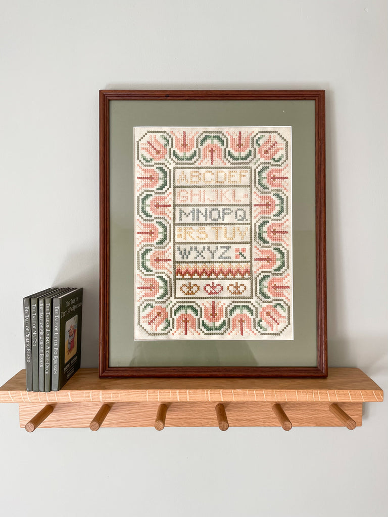 Vintage framed embroidery featuring an alphabet design in pastel colours with a green mount - Moppet