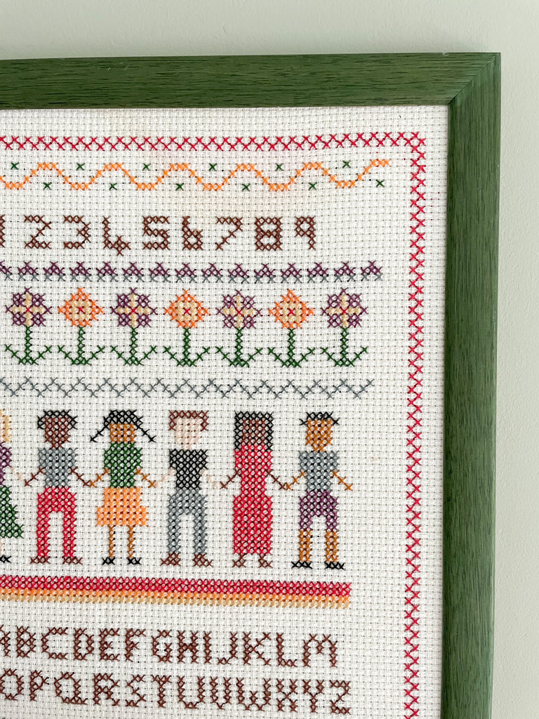 Vintage framed children's embroidery or needlework alphabet sampler featuring a row of children holding hands in a green wooden frame - Moppet