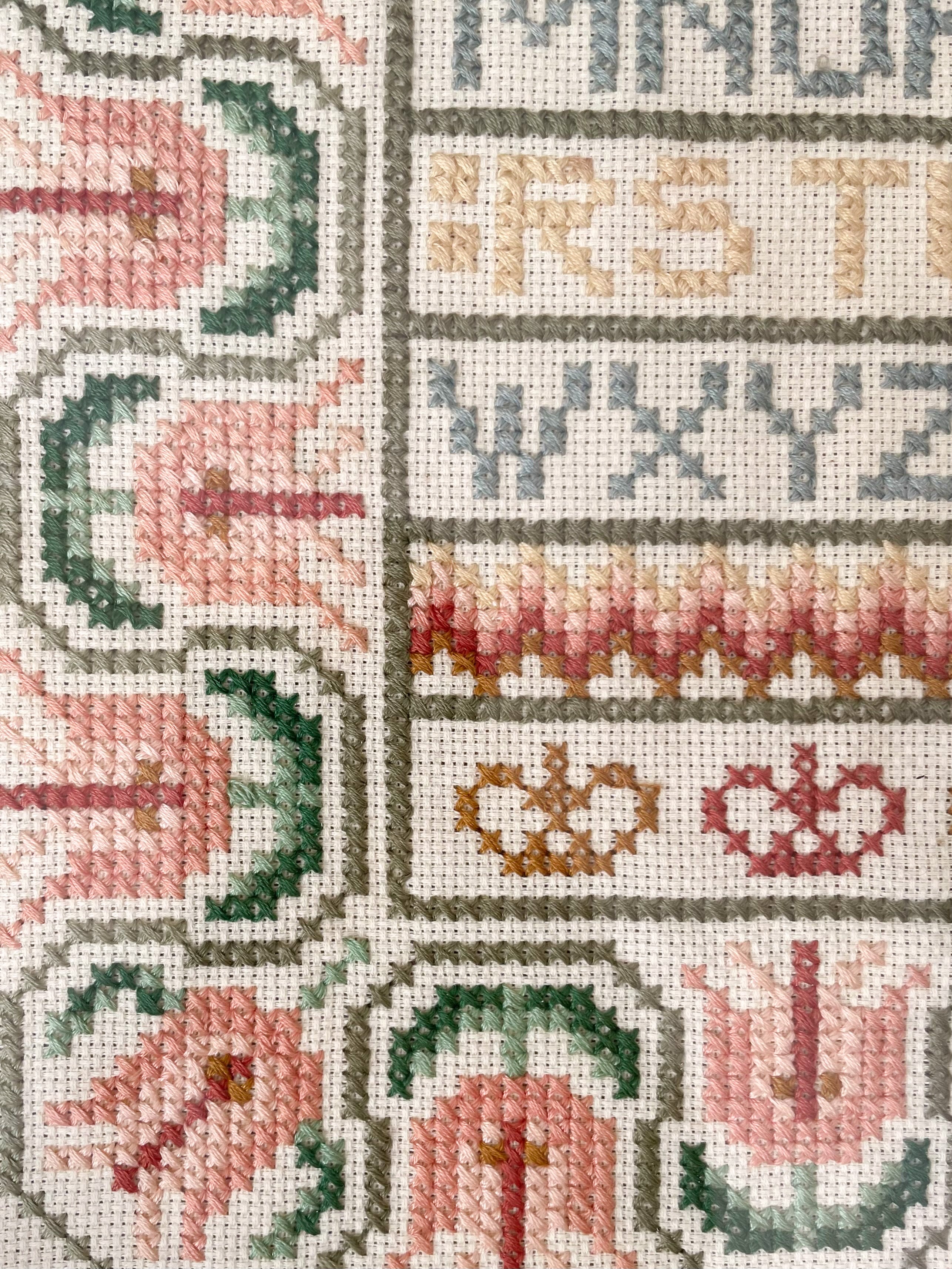 Vintage framed embroidery featuring an alphabet design in pastel colours with a green mount - Moppet